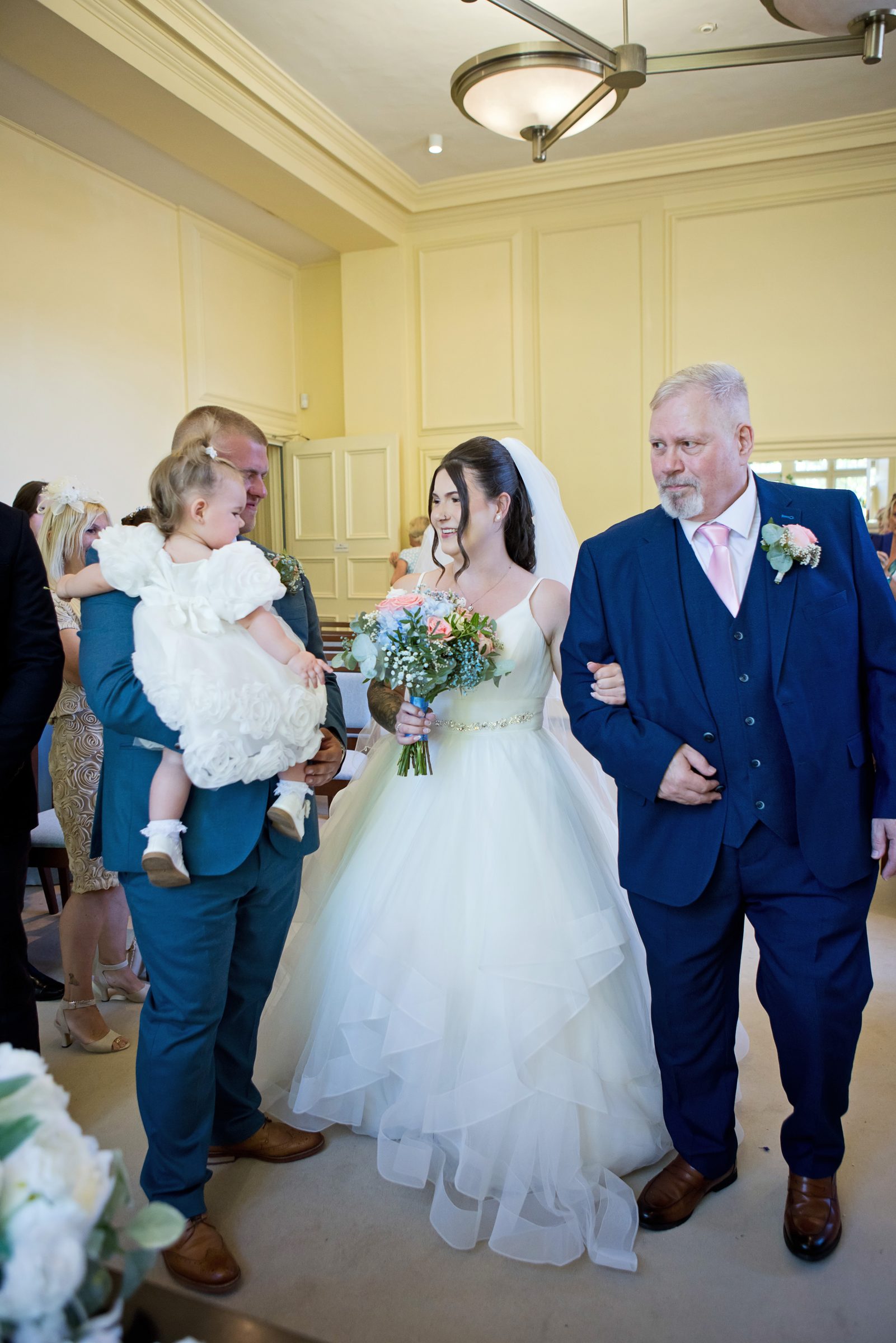 Melli walking into the ceremony with her bouquet, family beside her